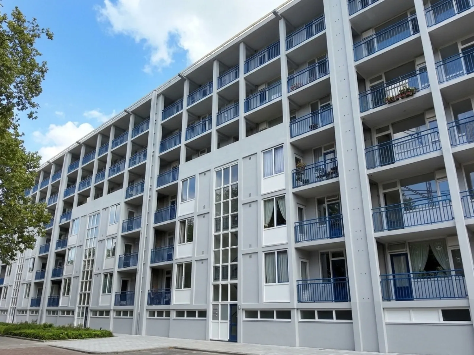 Hetzelfde complex na oplevering: strak wit geschilderde galerijen en kolommen, blauwe balkonhekken, steigers weg