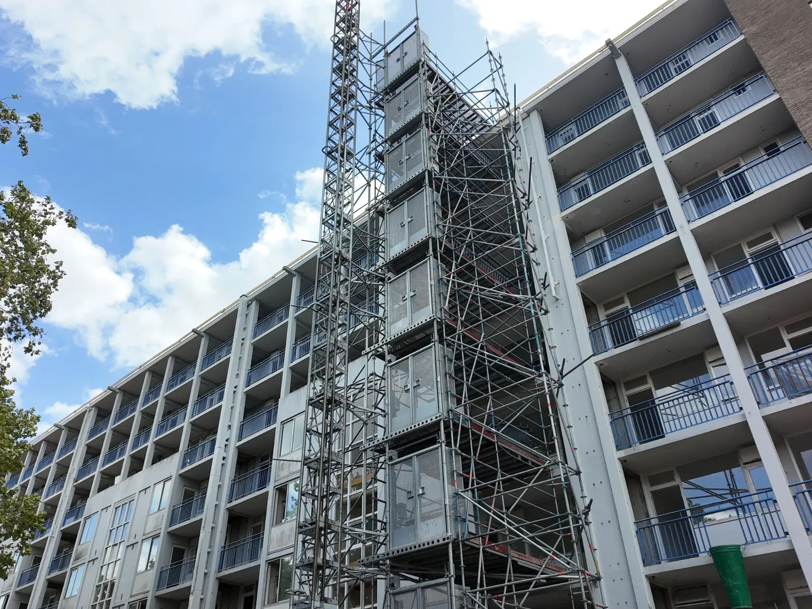 Appartementencomplex tijdens de renovatie: steigers en een bouwlift tegen de galerijen, de gevel nog dof en vervuild