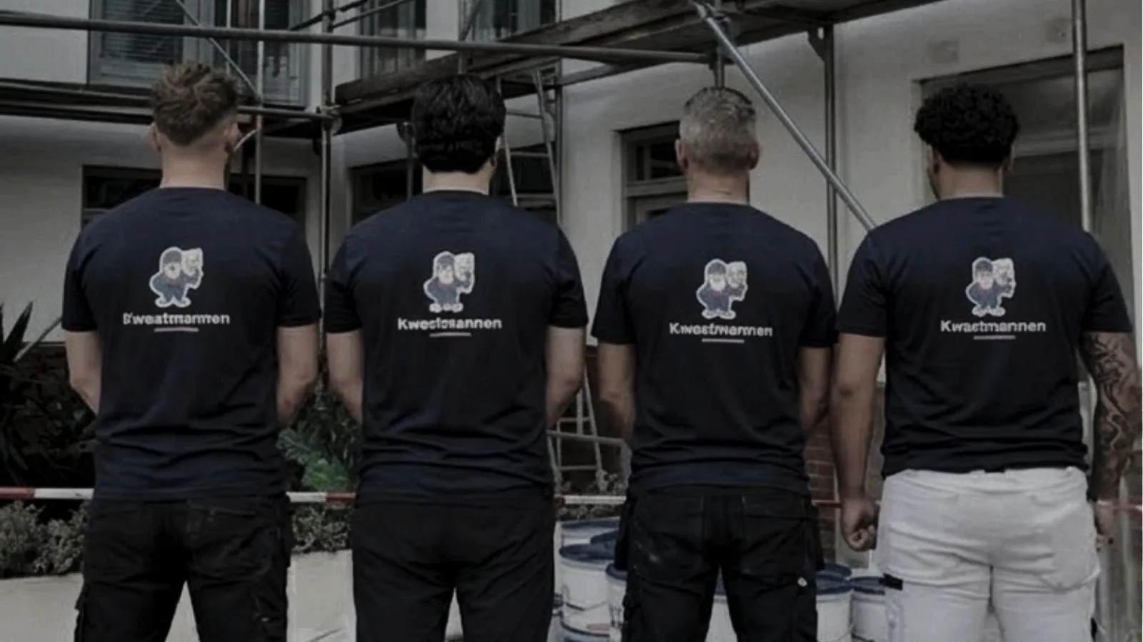 Vier schilders van Kwastmannen naast elkaar met het logo op de rug, voor een pand in de steigers met verfemmers op de grond