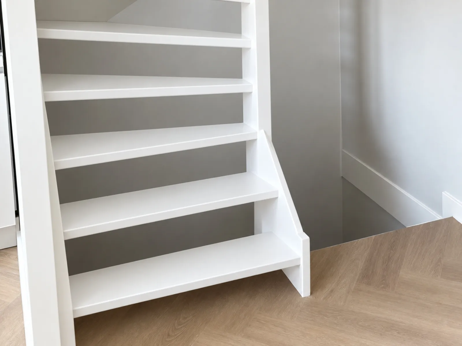 Wit gelakte houten trap met gladde treden en een strakke zijwang, tegen een grijze wand